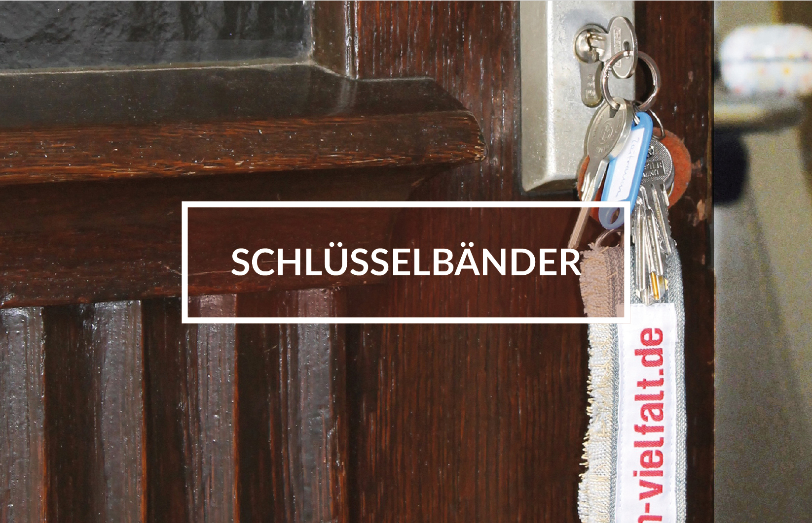 Geöffnete Tür mit Schlüssel im Schloss, Schlüsselband mit der Aufschrift:"vielfalt.de". In der Mitte des Bildes weiß gerahmter Kasten mit dem Schriftzug: "Schlüsselbänder".