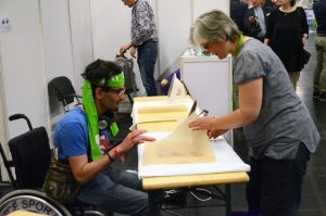 Ein Mitarbeiter im Rollstuhl erklärt die Wachstuch-Herstellung..